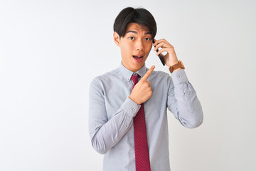 Chinese businessman wearing tie talking on the smartphone over isolated white background very happy pointing with hand and finger