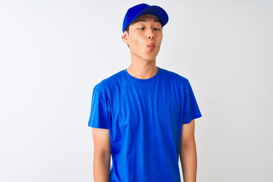 Chinese deliveryman wearing blue t-shirt and cap standing over isolated white background making fish face with lips, crazy and comical gesture. Funny expression.
