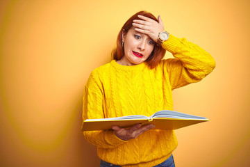 Young redhead student woman reading book standing over yellow isolated background stressed with hand on head, shocked with shame and surprise face, angry and frustrated. Fear and upset for mistake.