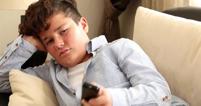 13 years old child boy watching tv sitting on a couch at home alone