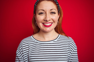 Beautiful redhead woman wearing striped navy t-shirt standing over isolated red background with a happy and cool smile on face. Lucky person.