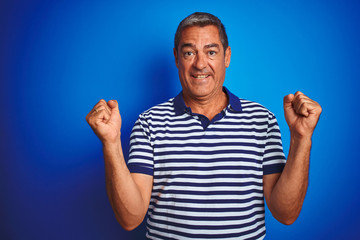 Handsome middle age man wearing striped polo standing over isolated blue background celebrating surprised and amazed for success with arms raised and open eyes. Winner concept.