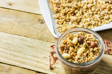 Homemade Granola Muesli with oats dried fruits coconut flakes hazelnuts almonds walnuts mixture on baking tray and in glass jar on rustic wood table. Healthy wholesome food fiber energy source