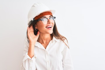 Young beautiful architect woman wearing helmet and glasses over isolated white background smiling with hand over ear listening an hearing to rumor or gossip. Deafness concept.