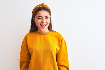 Young beautiful woman wearing yellow sweater and diadem over isolated white background winking...