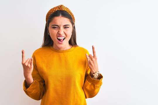 Young beautiful woman wearing yellow sweater and diadem over isolated white background shouting with crazy expression doing rock symbol with hands up. Music star. Heavy concept.