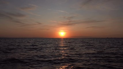 Quiet island at sunset. It shows fluffy clouds moving slowly towards the fading sun. The sun's golden-orange rays are reflected in the ocean, which is completely calm.