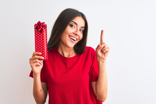 Young beautiful woman holding valentine gift standing over isolated white background very happy pointing with hand and finger to the side