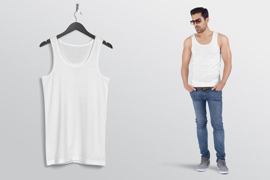 Hanging white plain tank top shirt on wall along with male model in blue denim jeans pant. Isolated background