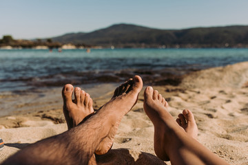 legs of a young woman and man lying on the beach on sunny summer day. feet of couple relaxing on...
