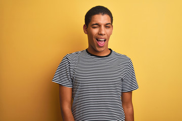 Young handsome arab man wearing navy striped t-shirt over isolated yellow background winking looking at the camera with sexy expression, cheerful and happy face.