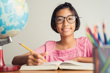 Asian girl with glasses is taking notes in her class notebook, Educational concept