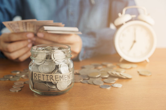 A coin in a glass bottle Image blurred background of business people sitting counting money and a retro white alarm clock, finance and saving money for future concept.