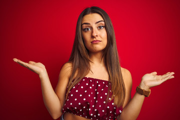 Young beautiful woman wearing casual t-shirt standing over isolated red background clueless and...
