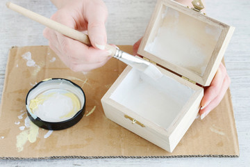Woman paints on white color a wooden box.