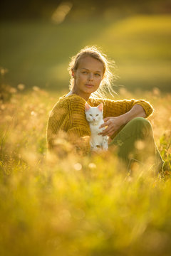 Pretty, Young Woman With Her Cat Pet Sitting In Grass On Lovely Meadow Lit By Warm Evening Light (shallow DOF; Color Toned Image)