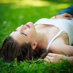 Close-up portrait of an attractive young woman outdoors, lying in the grass.