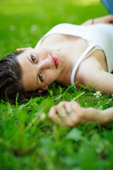 Close-up portrait of an attractive young woman outdoors, lying in the grass.