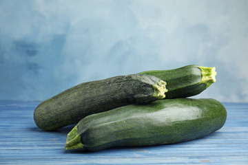 Fresh ripe green zucchinis on wooden table against blue background, space for text