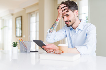 Young business man using touchpad tablet stressed with hand on head, shocked with shame and surprise face, angry and frustrated. Fear and upset for mistake.