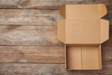 Open cardboard box on wooden background, top view. Space for text