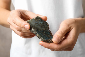 Young woman holding beautiful labradorite gemstone on beige background, closeup