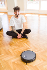 Young man using automatic vacuum cleaner to clean the floor, controling machine housework robot