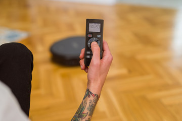 Close up of man hands controling automatic vacuum cleaner using electronic control of the mopping...