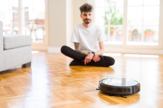 Young man using automatic vacuum cleaner to clean the floor, controling machine housework robot