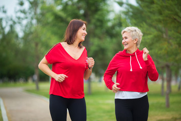 two adult women in sportswear run in the summer park