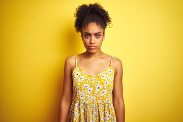 African american woman wearing casual floral dress standing over isolated yellow background skeptic...