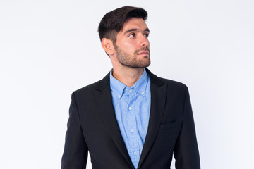 Portrait of young bearded Persian businessman in suit thinking and looking up