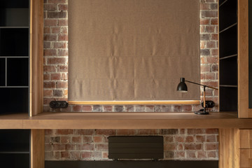 Custom-made timber table with lamp and bookcase with shelves against brick wall and window with...