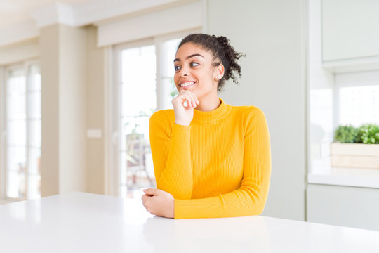 Beautiful african american woman with afro hair wearing a casual yellow sweater with hand on chin thinking about question, pensive expression. Smiling and thoughtful face. Doubt concept.