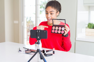 Young african american influencer woman recording make up tutorial very happy pointing with hand...