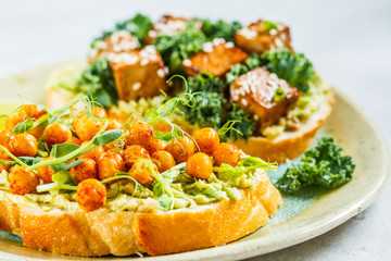 Vegan open sandwiches with guacamole, tofu, chickpeas and sprouts on a plate.