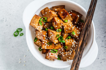 Fried tofu in teriyaki sauce in white bowl, top view. Vegan food concept.