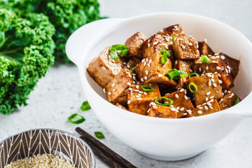 Teriyaki tofu with sesame seeds and green onion in white bowl. Vegan food concept.