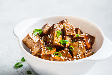 Teriyaki tofu with sesame seeds and green onion in white bowl. Vegan food concept.