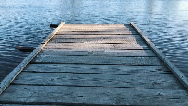 Cool view on tranquil blue water in the lake from an old wooden pier/bridge in Slow motion