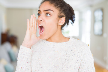 Fototapeta na wymiar Beautiful young african american woman with afro hair wearing casual sweater shouting and screaming loud to side with hand on mouth. Communication concept.