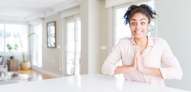 Wide angle of beautiful african american woman with afro hair praying with hands together asking for forgiveness smiling confident.