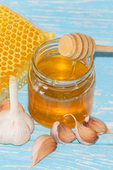 Honey and pieces of garlic on the background of honeycomb. Honey in a glass jar and honeycomb.