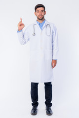 Full body shot of young bearded Persian man doctor pointing up