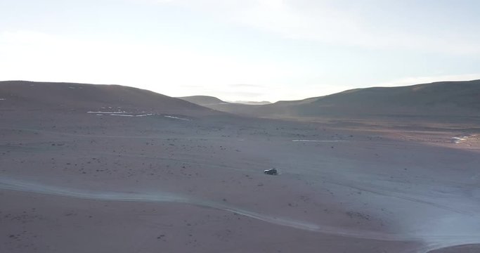 A smooth drone shot filmed in Bolivia during sunrise showing an offroad vehicle driving on an unpaved road.
