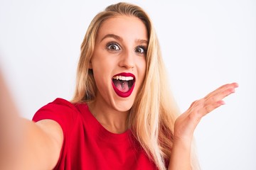 Young beautiful woman wearing t-shirt make selfie by camera over isolated white background very happy and excited, winner expression celebrating victory screaming with big smile and raised hands