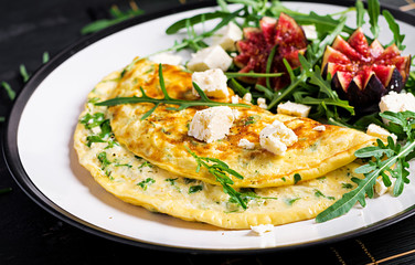 Omelette with feta cheese, parsley and salad with figs, arugula on white plate. Frittata - italian omelet.