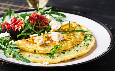 Omelette with feta cheese, parsley and salad with figs, arugula on white plate. Frittata - italian omelet.