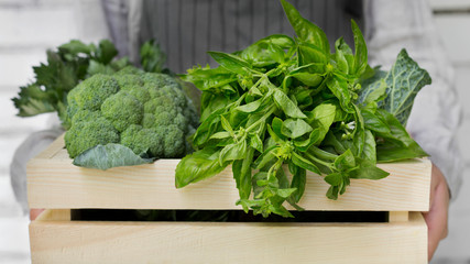 Woman holding broccoli and greens in organic wooden box