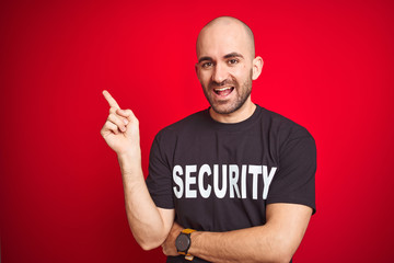 Fototapeta premium Young safeguard man wearing security uniform over red isolated background with a big smile on face, pointing with hand and finger to the side looking at the camera.